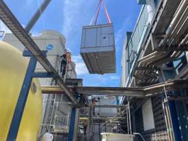 A new evaporative condenser unit lifted by crane into a plant's equipment area