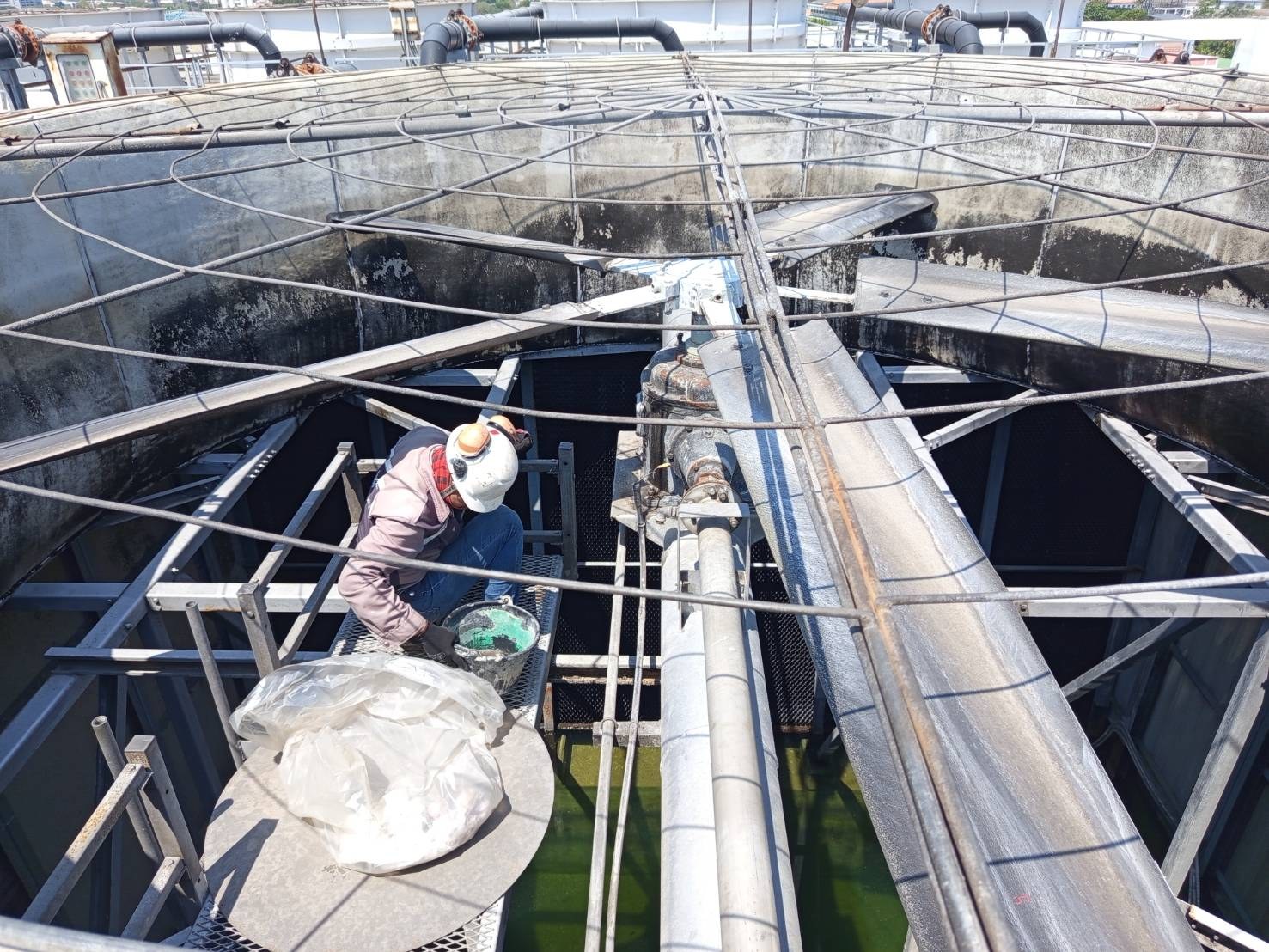 Technician working on the top deck of a cooling-tower cell at the site, beside the water-distribution header and fill packs